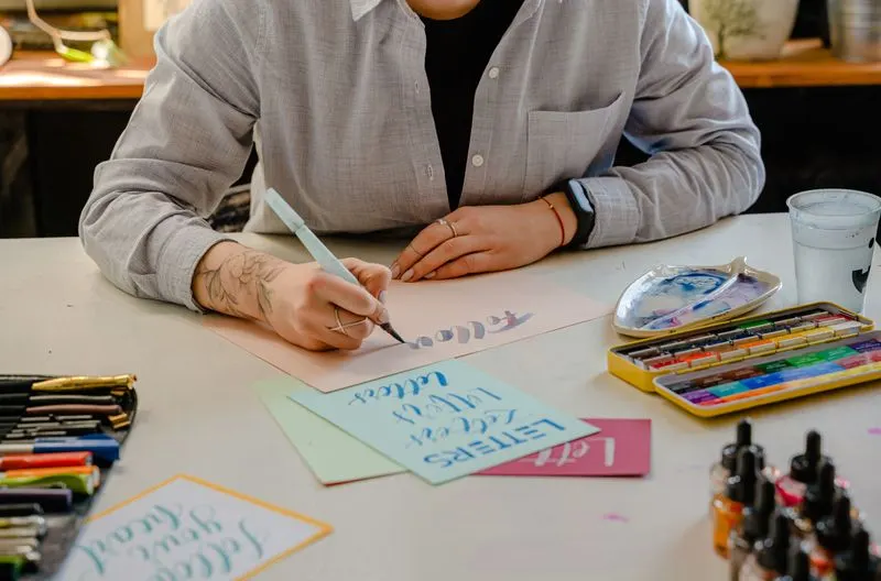 Person lettering with brush pens and inks on a desk